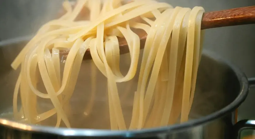 Gorący makaron mie unoszony na drewnianej łyżce nad parującym garnkiem. Idealny przepis na szybki obiad.