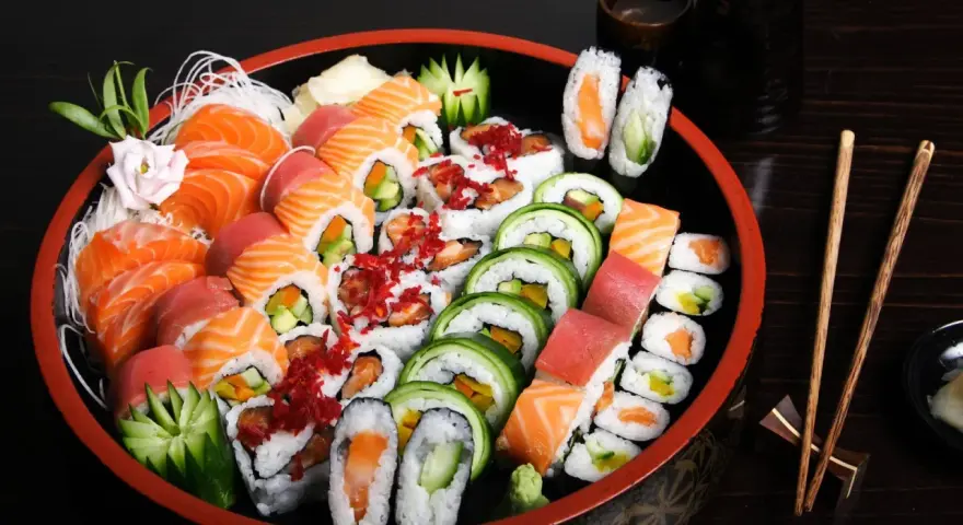 Talerz pełen różnorodnych sushi, w tym nigiri z łososiem i tuńczykiem, rolki z ogórkiem i awokado, a także kilka kawałków temaki sushi.