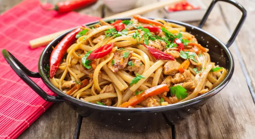 Pyszny makaron chain main z kurczakiem, papryką i chili, posypany natką pietruszki, w czarnej woku.