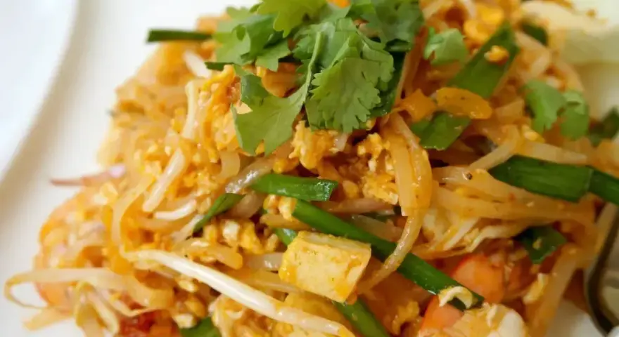 Pyszne phat thai z krewetkami, jajkiem i szczypiorkiem, udekorowane świeżą kolendrą.