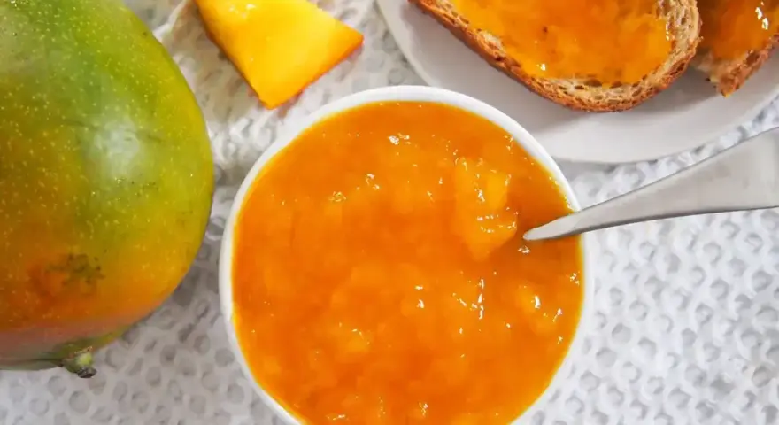 Słoik z dżemem z mango, obok świeży owoc i kromki chleba. Codzienne jedzenie mango to pyszny początek dnia.