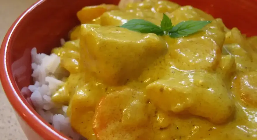 Miseczka ryżu z kurczakiem w kremowym sosie z curry, ozdobiona listkiem mięty.