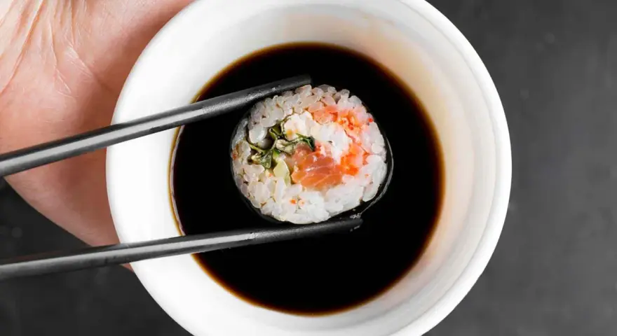 Pałeczkami zanurzam rolkę sushi w ciemnym sosie. Idealny sos słodki do sushi podkreśla smak ryby i ryżu.