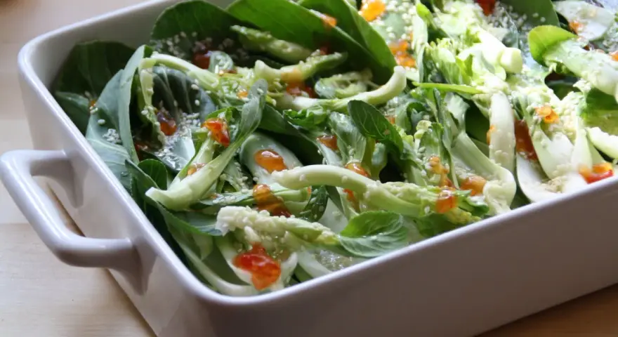 Pyszna kapusta pak choi po tajsku, polana sosem i posypana sezamem, w białej ceramicznej misie.