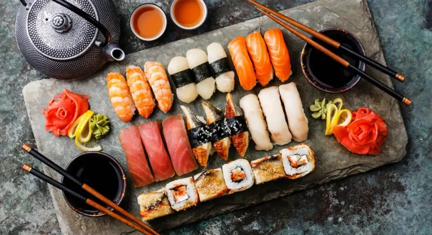 Zestaw sushi: nigiri z łososiem, krewetkami, tuńczykiem, węgorzem i rolki. Obok czajniczek, miseczki z herbatą i sos sojowy. Tak jedzą japończycy.