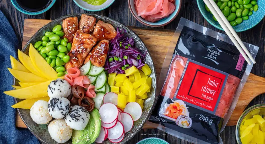 Kolorowy bowl z kawałkami glazurowanego lososia, ryżem, awokado, mango, ogórkiem, rzodkiewką, edamame i marynowanym imbirem. Obok opakowanie różowego imbiru.
