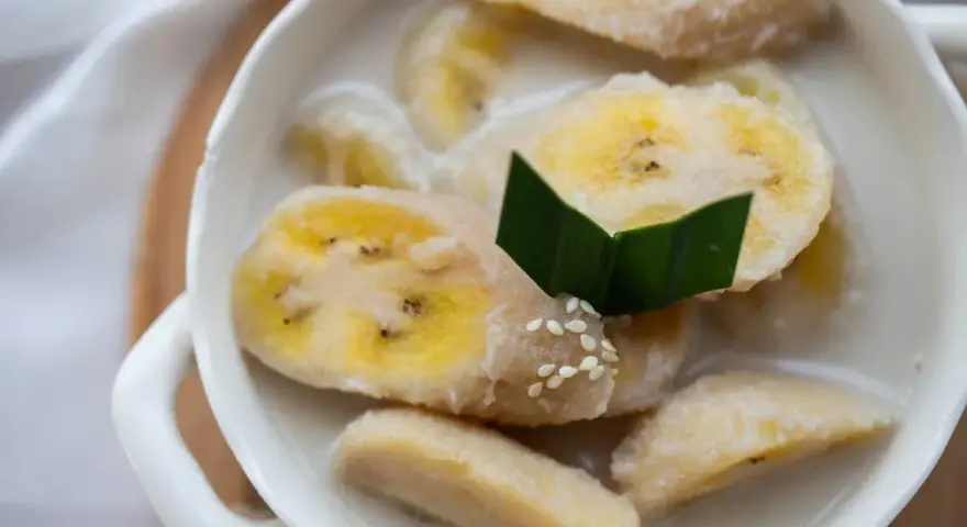 Kawałki banana w mleku kokosowym, ozdobione liściem pandanu i sezamem. Pyszny tajski deser.