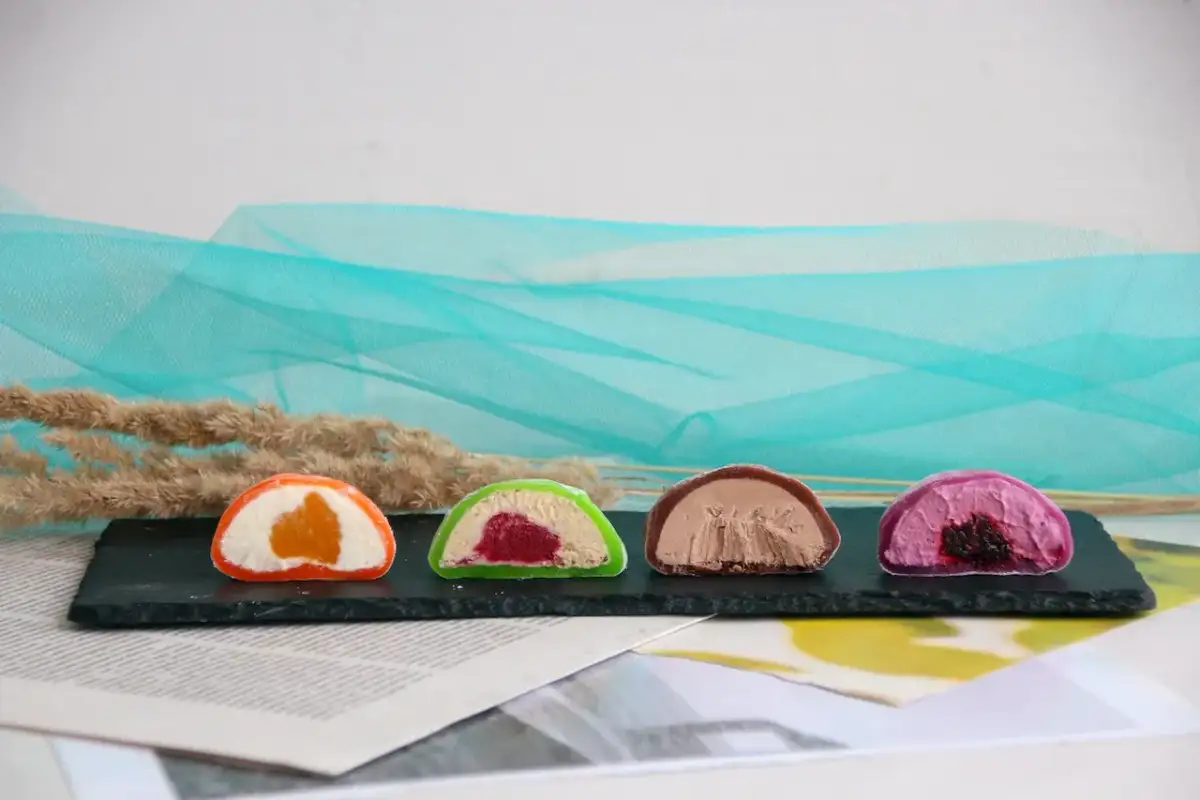 Cztery kolorowe mochi: pomarańczowe, zielone z malinami, czekoladowe i fioletowe z jagodami. Różne rodzaje słodkości.