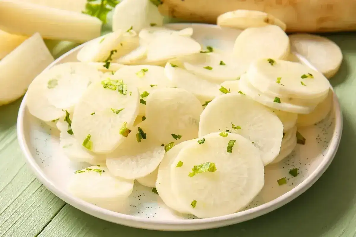 Plasterki białej rzodkwi, czyli daikon, posypane zielonymi ziołami na talerzu.