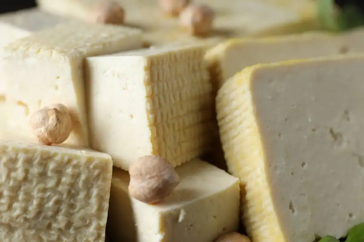 Kawałki miękkiego tofu ułożone obok siebie, niektóre z nich mają kratkowaną fakturę. Kilka ciecierzycy dodaje uroku.