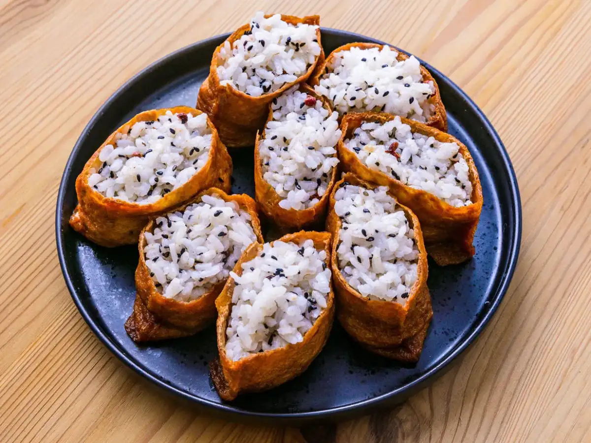 Tofu inari z ryżem i czarnym sezamem na czarnym talerzu.