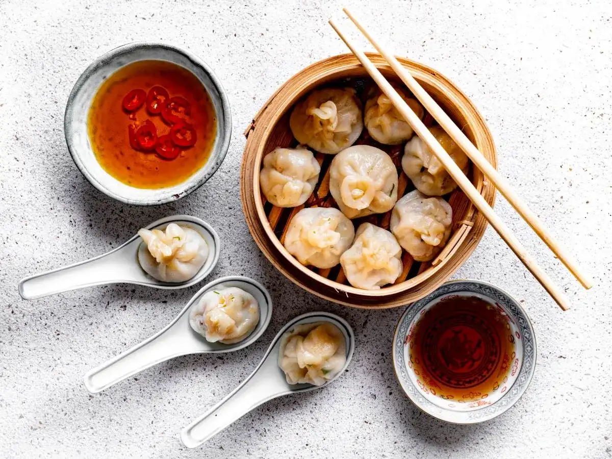 Pyszne dim sum w bambusowym parowniku, podane z sosem chili i sosem sojowym. Trzy pierożki na łyżeczkach zachęcają do spróbowania.