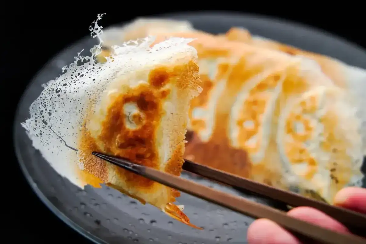 Chrupiące pierogi gyoza z delikatną, koronkową panierką, podniesione pałeczkami.