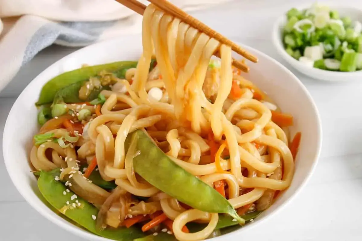 Pyszne udon teriyaki z groszkiem cukrowym i marchewką, podane z sezamem.