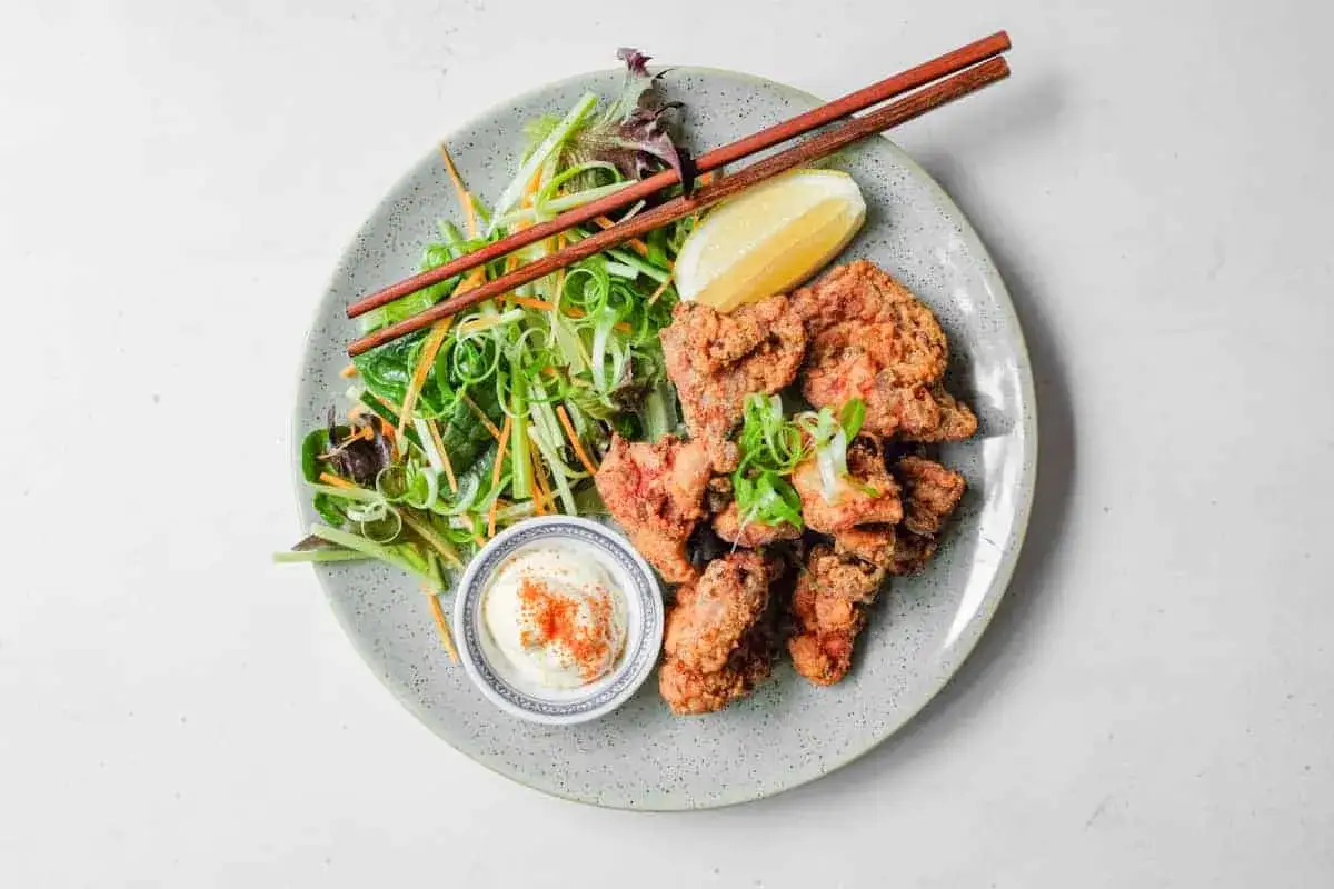 Chrupiące karaage chicken z sosem, sałatką i cytryną na talerzu. Pałeczki czekają na smaczny posiłek.