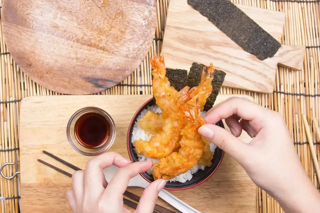 Ręce układają chrupiące krewetki tempura na ryżu. Idealny przepis na tempurę, by poczuć smak Japonii.