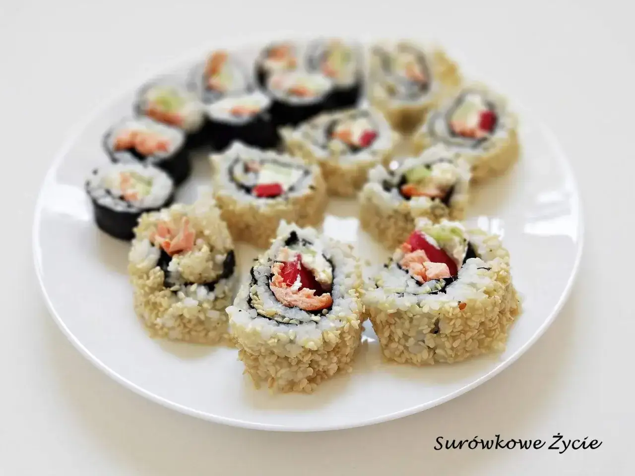 Talerz pełen pysznego sushi uramaki z łososiem, awokado i papryką, posypane sezamem.