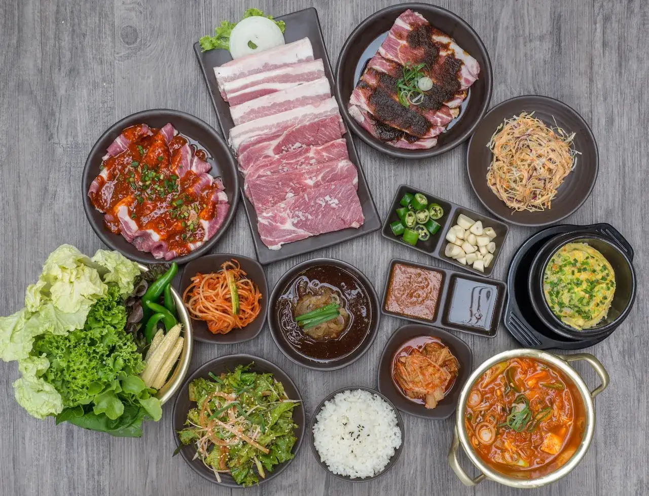 Obfity koreański obiad: surowe i marynowane mięso, kimchi, sałatki, ryż, zupy i dodatki.