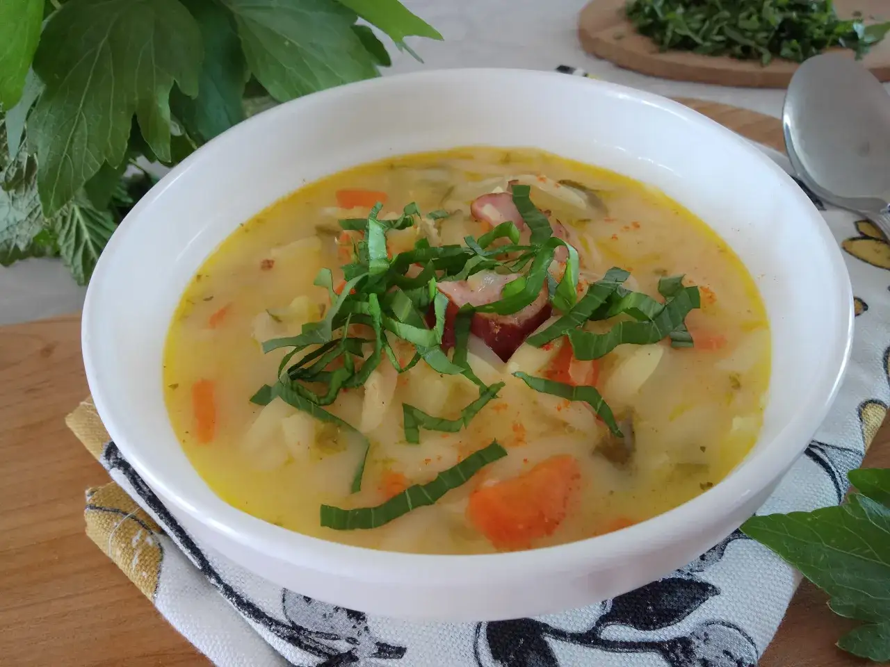 Aromaticzna zupa słodko kwaśna z kawałkami kiełbasy, ziemniaków i marchewki, udekorowana świeżymi ziołami.