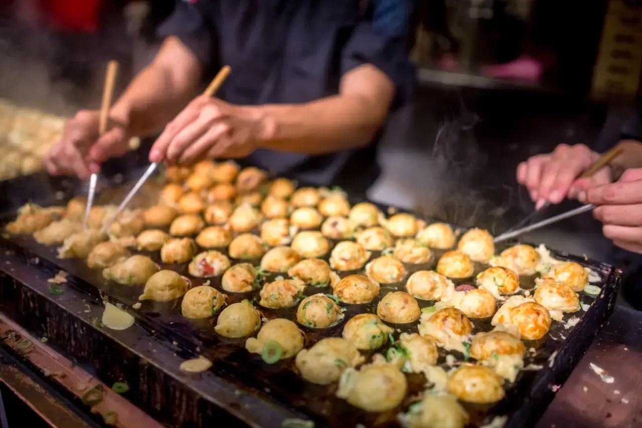 Ręce obracają gorące kulki takoyaki na płycie. Pyszny japoński street food prosto z ulicy.