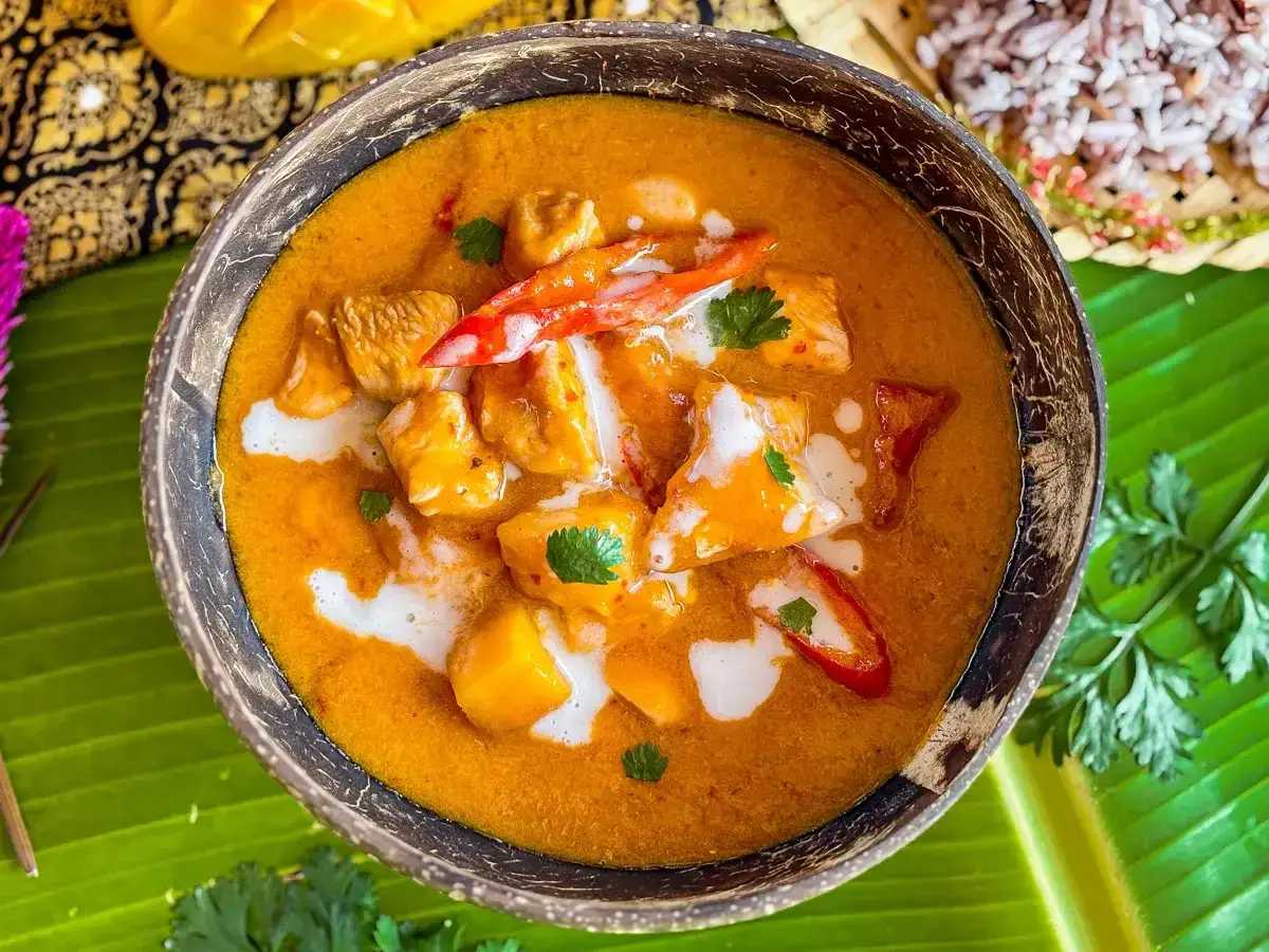 Aksamitny kurczak w sosie mango, ozdobiony chili i kolendrą, podany w misce z łupiny kokosa.