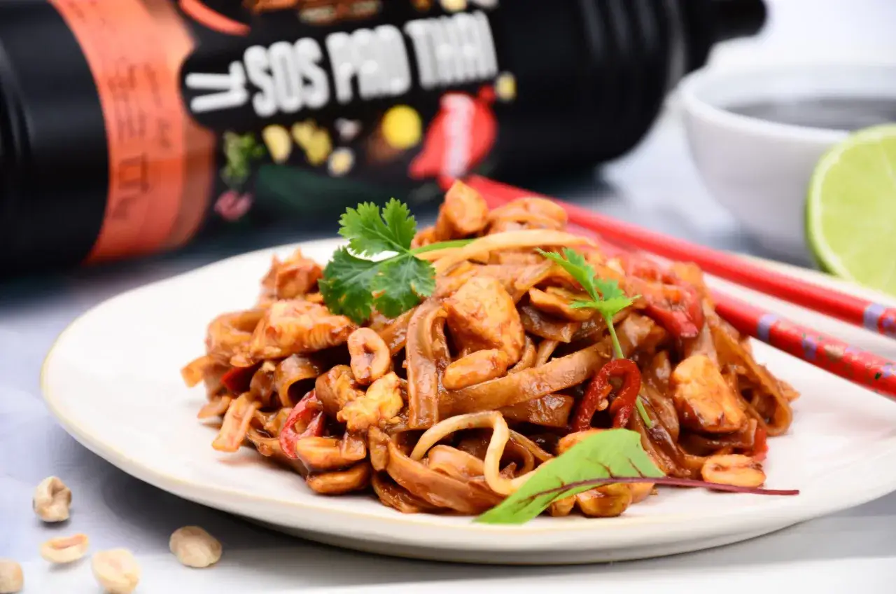 Prosty pad thai z kurczakiem na talerzu, z sosem w tle i pałeczkami. Smaczne danie azjatyckie.
