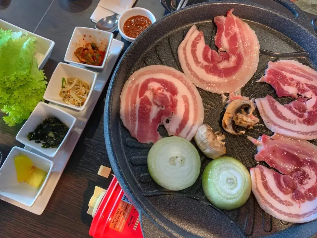 Pyszne plastry boczku na grillu, gotowe do przygotowania w stylu korean bbq. Obok sałatka, kimchi i inne dodatki.