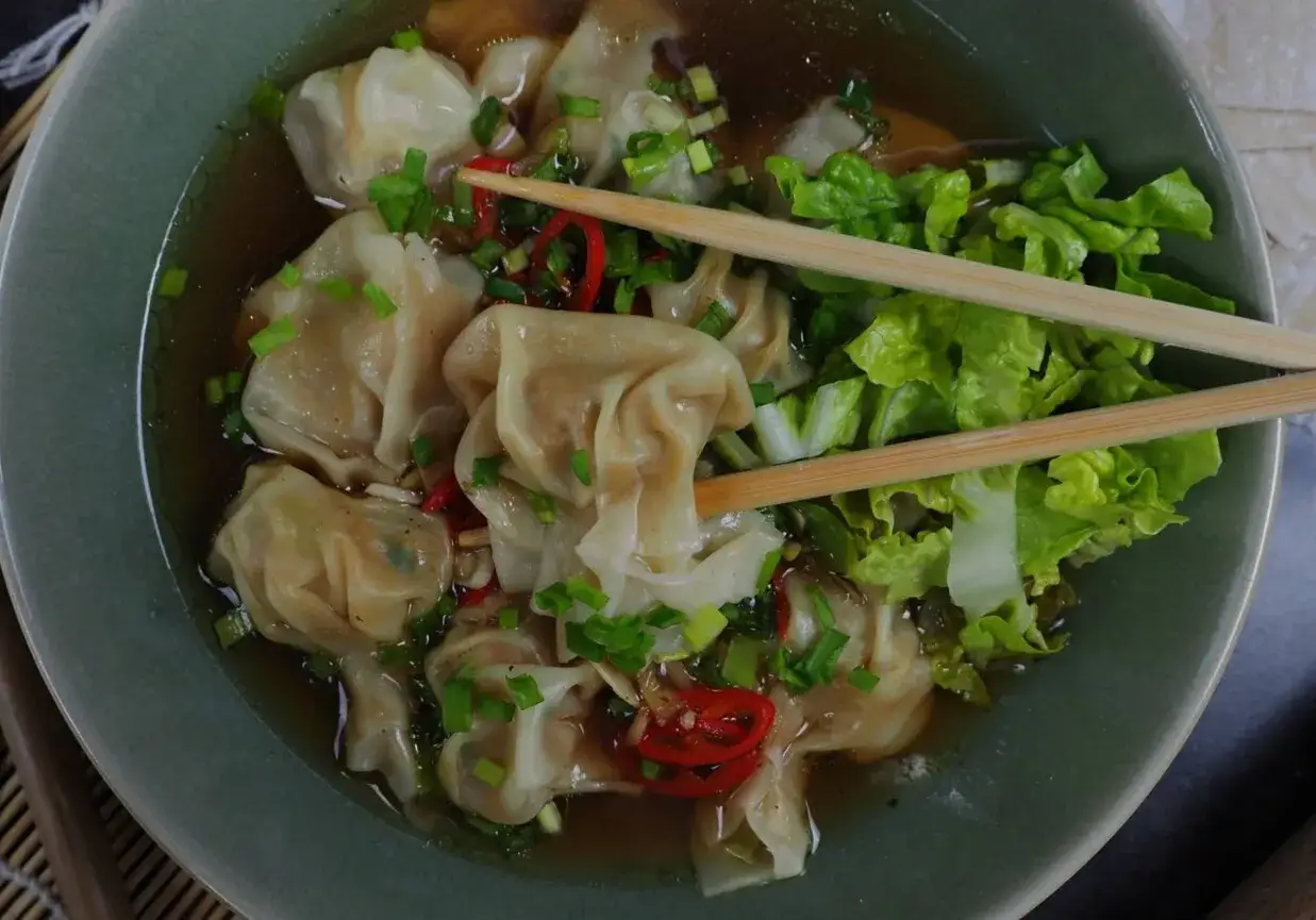 Pyszne chińskie zupy z pierożkami wonton, posypane szczypiorkiem i papryczką chili, podane z chrupiącą sałatą.