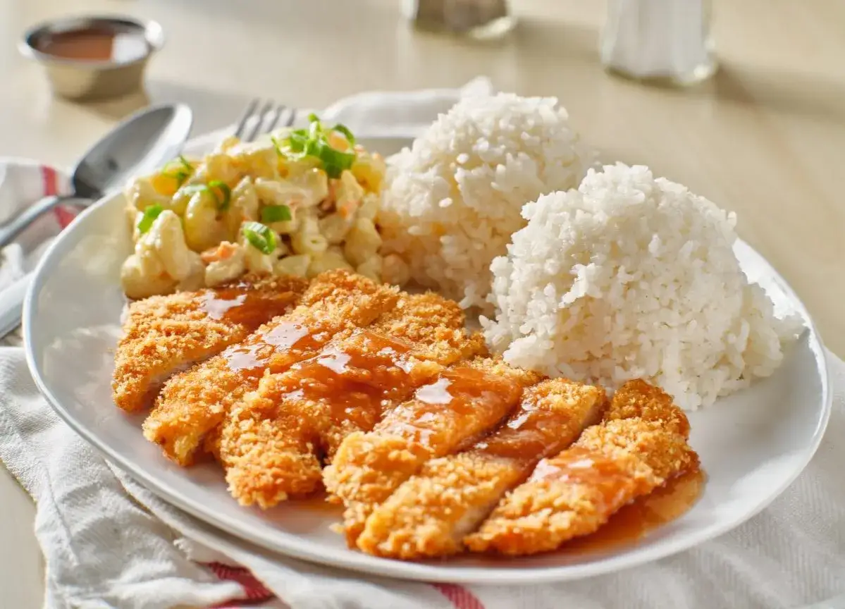 Chrupiące kotlety panierowane w panko, polane sosem, z porcją ryżu i sałatką makaronową.