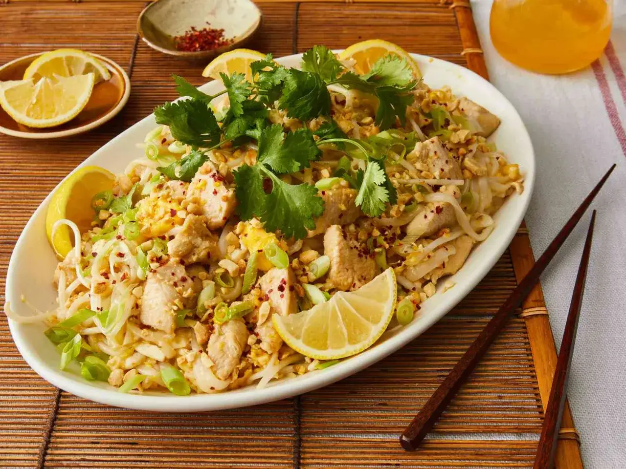 Pyszny pad thai co to? Danie z kurczakiem, makaronem ryżowym, orzeszkami ziemnymi, szczypiorkiem i kolendrą, udekorowane cytryną.