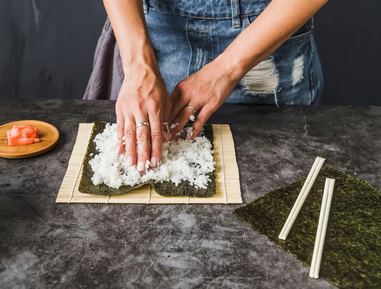 Dłonie rozprowadzają ryż na nori, przygotowując się do zwinięcia sushi. Zastanawiasz się, ile octu do sushi?