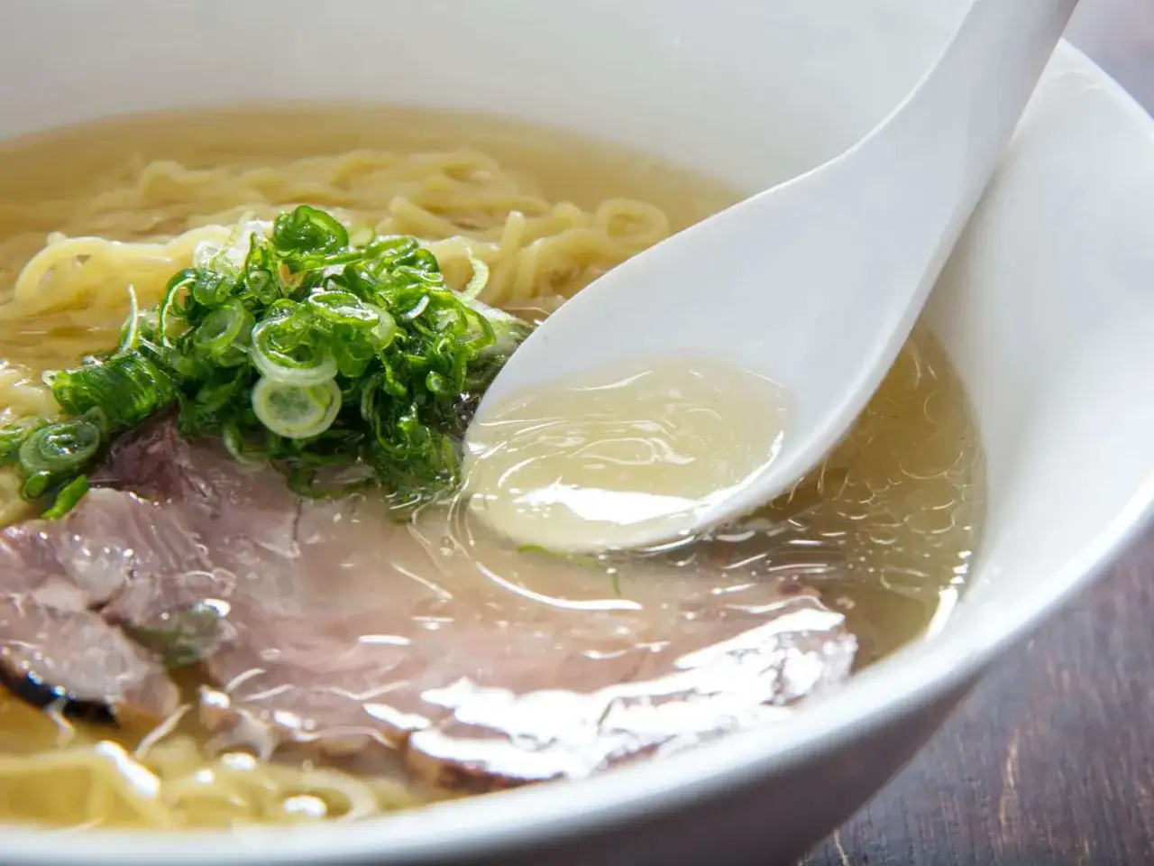 Chintan ramen z delikatnym bulionem, makaronem, plastrami wieprzowiny i zieloną cebulką. Łyżka zanurzona w aromatycznym wywarze.