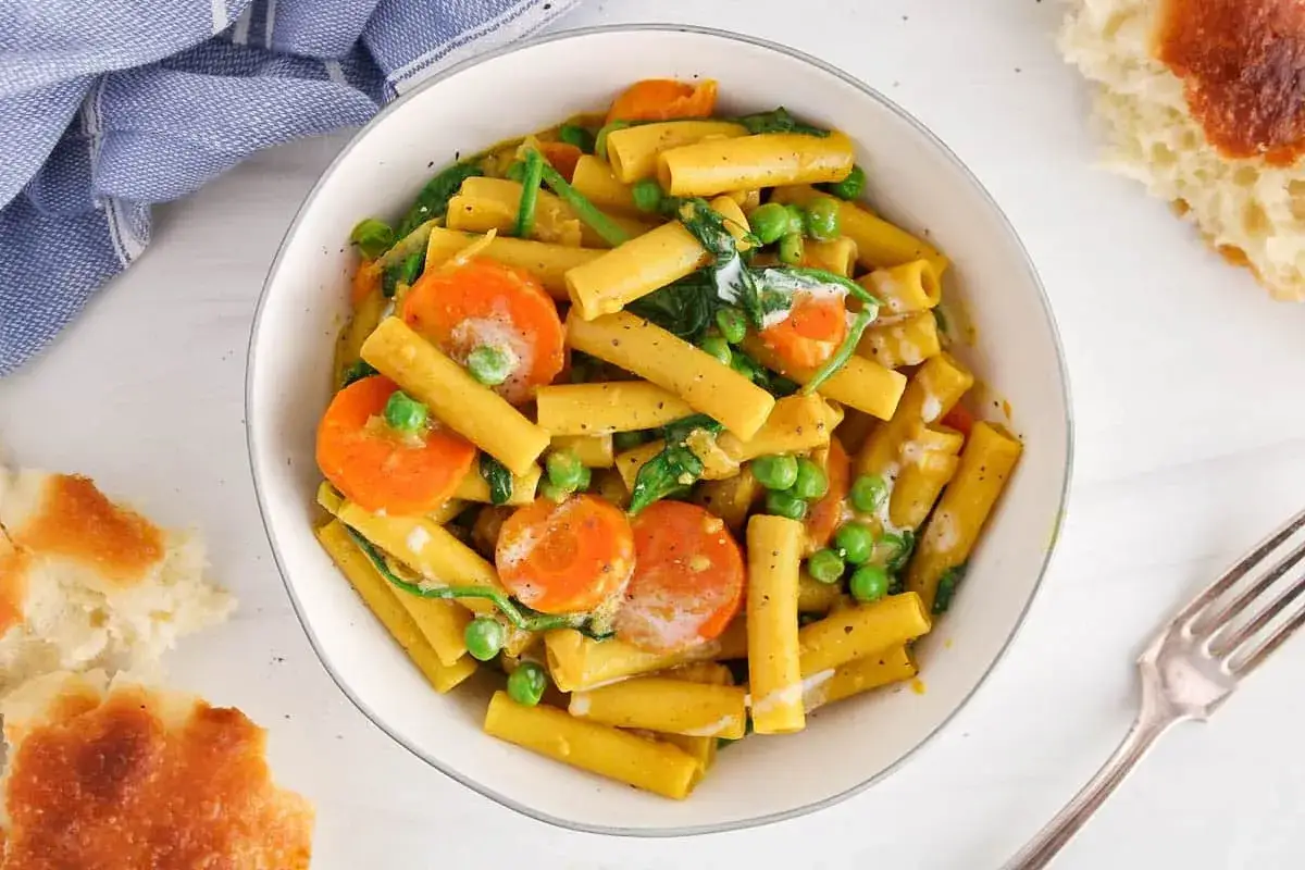 Pyszny makaron curry z marchewką i groszkiem w kremowym sosie, podany z chlebem.