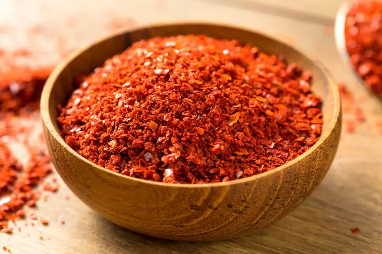 Drewniana miska pełna czerwonego, pikantnego gochugaru. To koreańska papryka chili w płatkach, idealna do kimchi i innych dań.