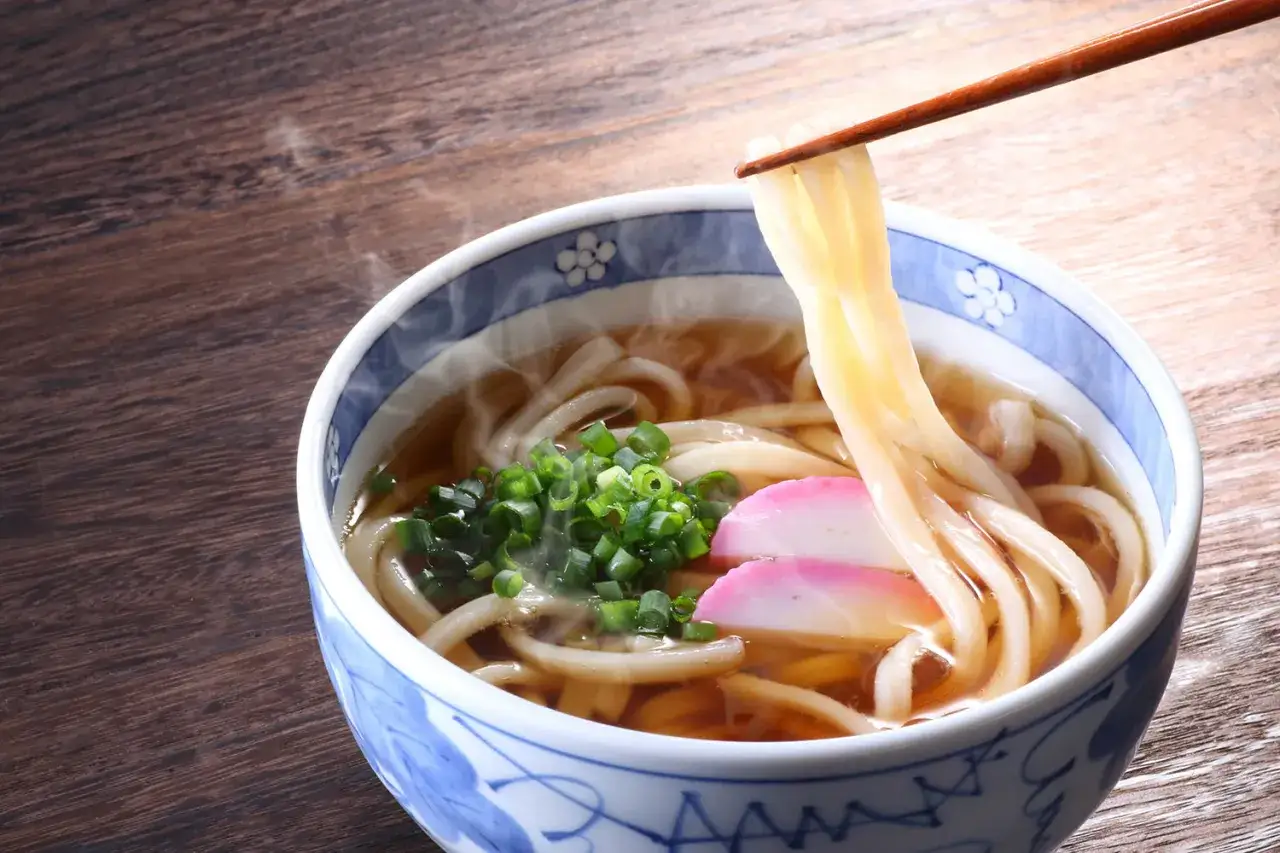 Parujące miseczka z grubym makaronem udon w aromatycznym bulionie, posypana szczypiorkiem i kawałkami rybnej pasty. Idealne na rozgrzewający posiłek.