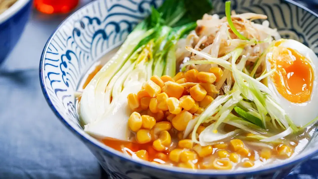 Miseczka aromatycznego ramen miso z jajkiem na pół, kukurydzą, pak choi i kiełkami fasoli.