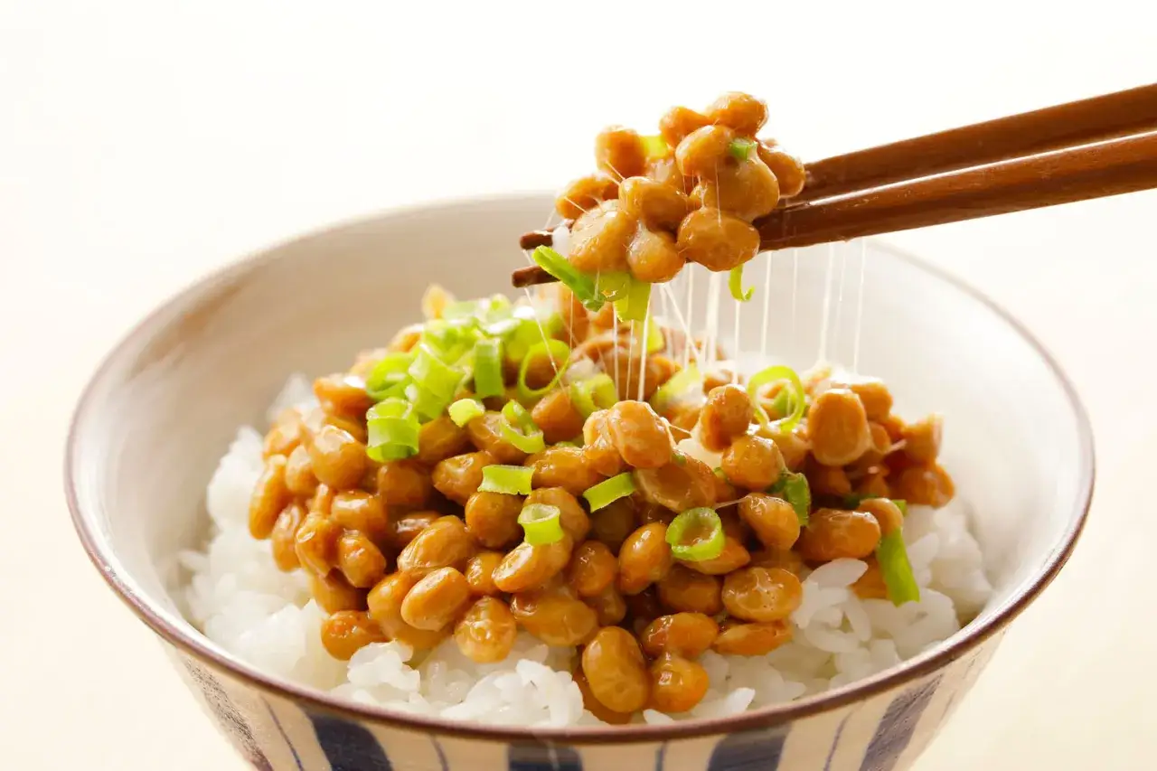 Miseczka ryżu z natto, japońską potrawą z fermentowanej soi, posypana szczypiorkiem. Pałeczki unoszą nitki natto.