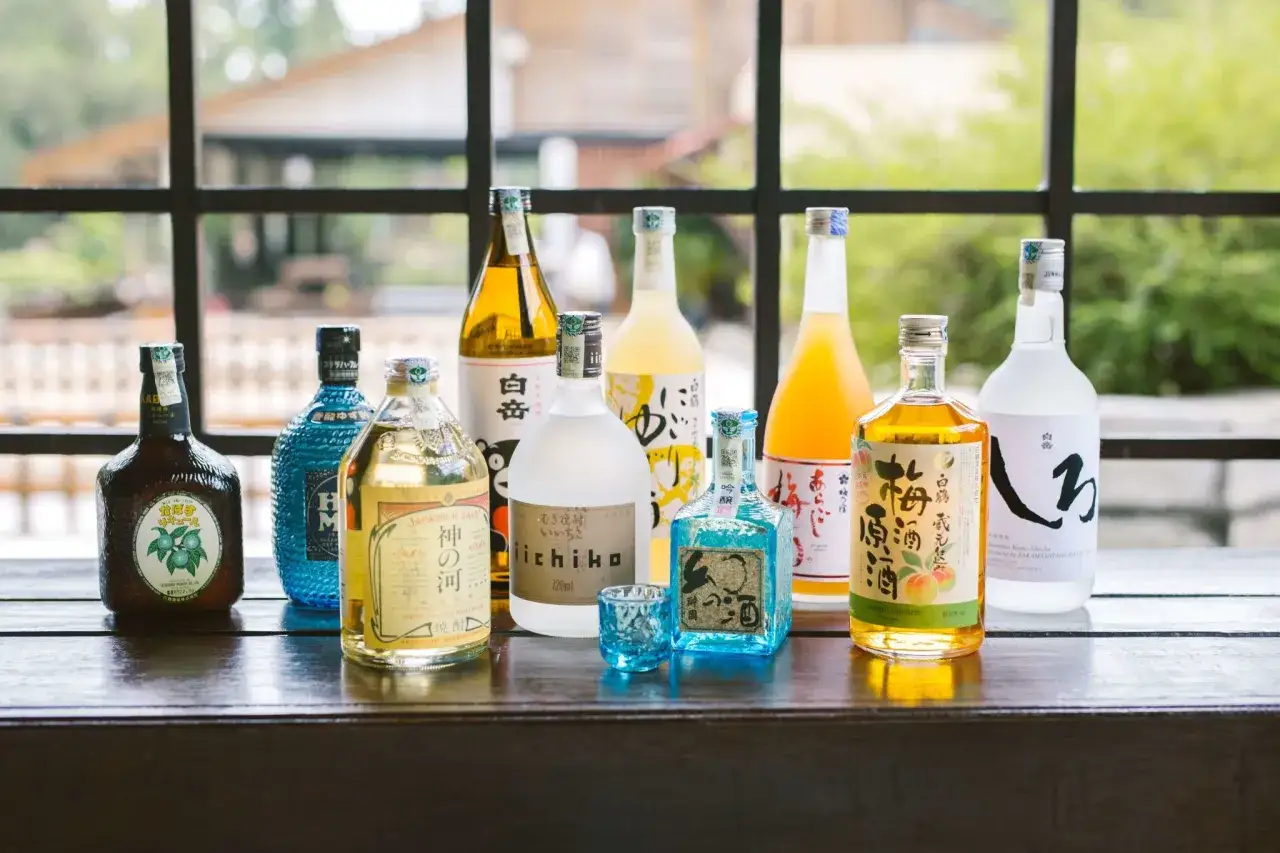 Rząd butelek z japońskim alkoholem, w tym sake i shochu, ustawiony na drewnianym stole.