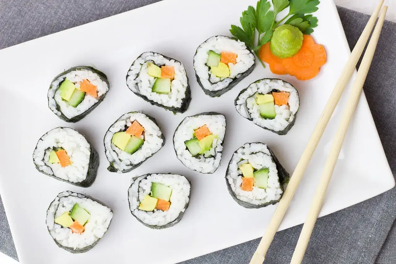 Pyszne futomaki przepis na talerzu: rolki sushi z awokado, ogórkiem i marchewką, udekorowane wasabi i natką pietruszki.