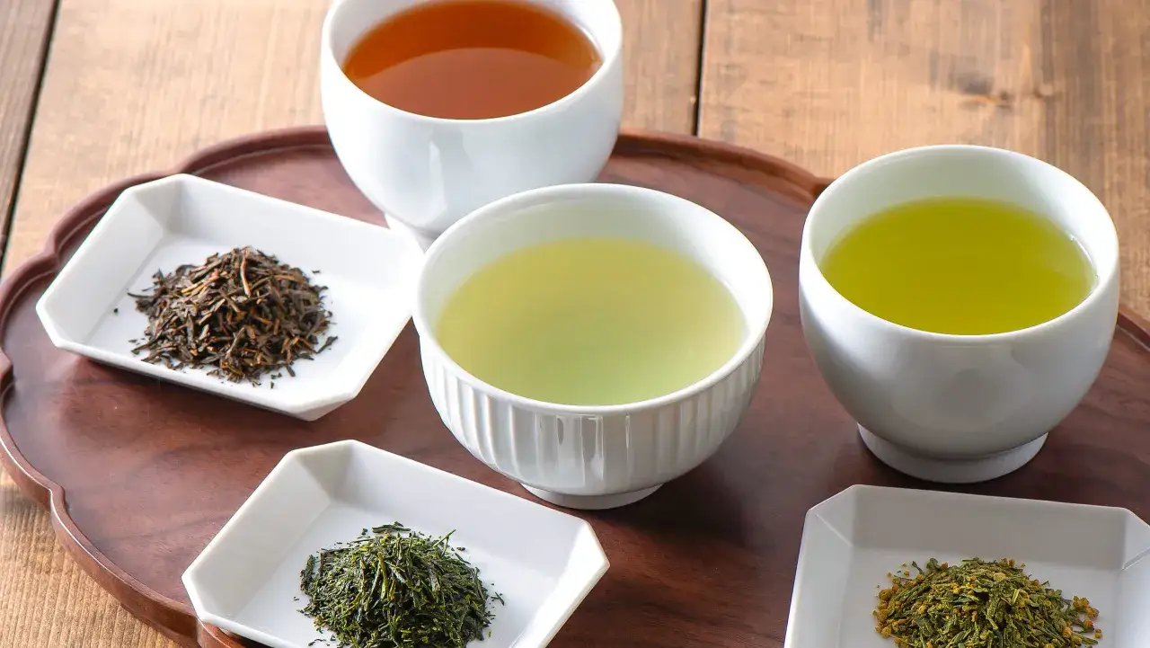 Różne rodzaje zielonej herbaty: sencha, genmaicha i inne, podane w białych miseczkach.