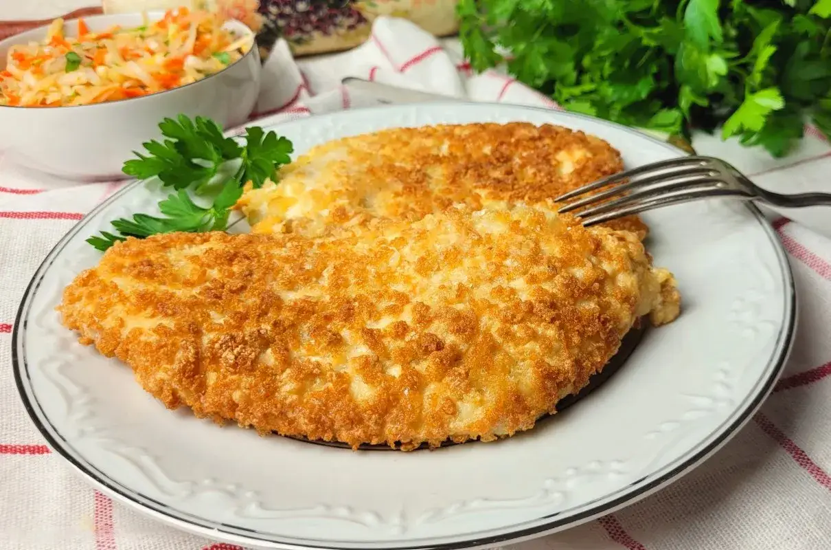 Chrupiący kurczak w panko na talerzu, udekorowany natką pietruszki. Obok miseczka z surówką.
