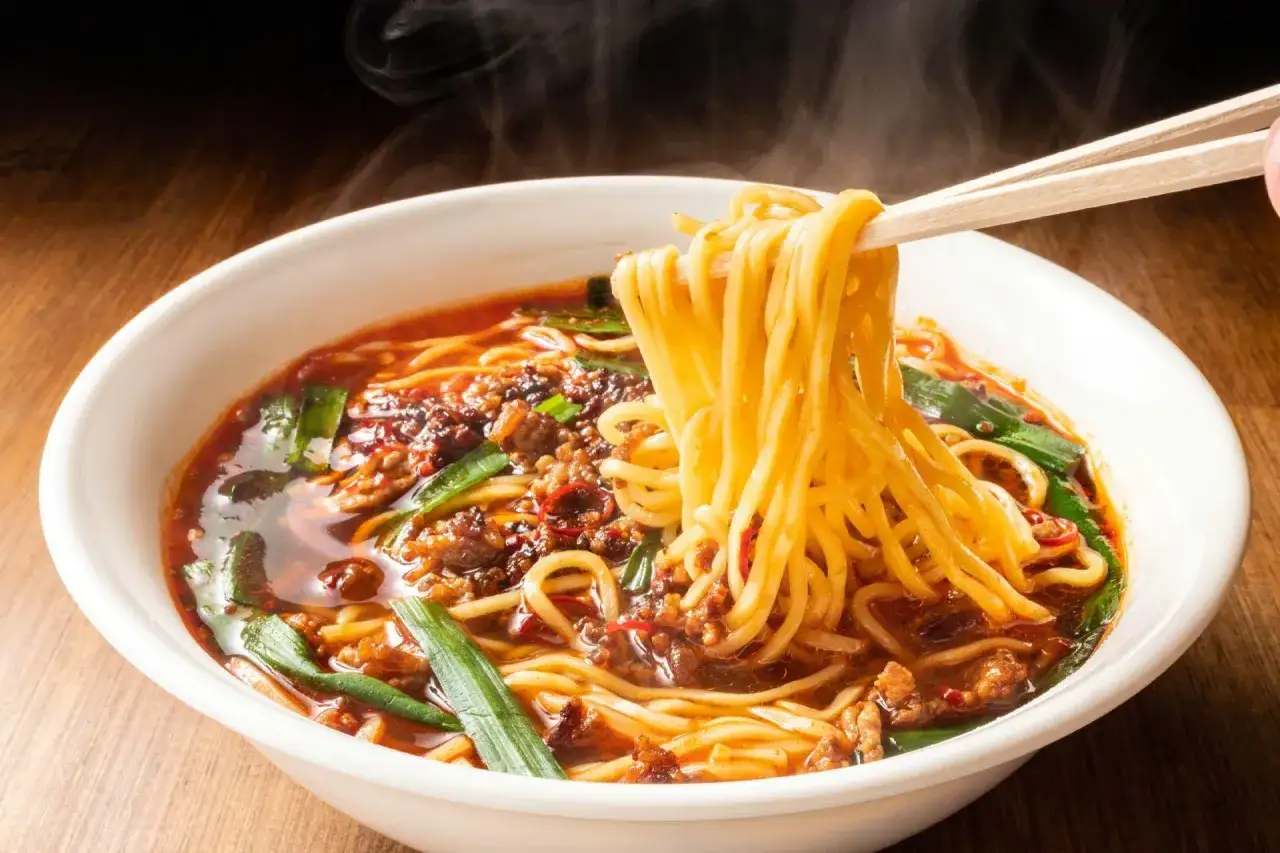 Gorąca zupa ramen z parującym bulionem, mięsem mielonym i zieloną cebulką, podana w białej misce.