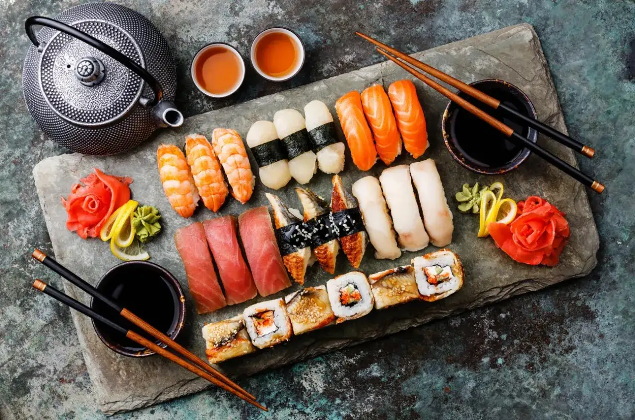 Japonia tradycje: bogactwo sushi, od krewetek po łososia, z imbirem i wasabi, podane z czajniczkiem i dwoma filiżankami herbaty.