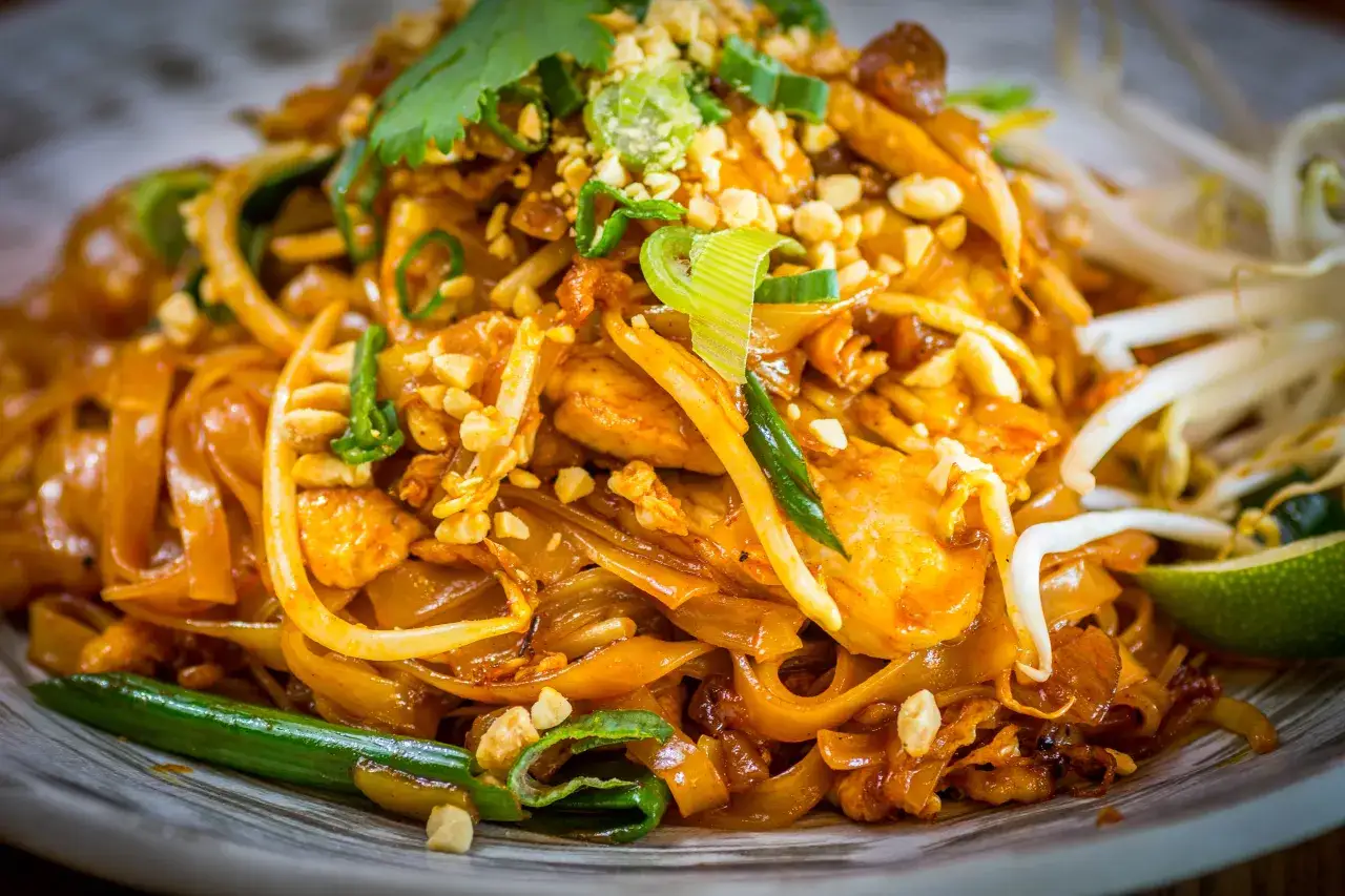 Pyszne pad thai z warzywami, posypane orzeszkami ziemnymi i szczypiorkiem. Kolorowe danie z makaronem ryżowym, kurczakiem i kiełkami fasoli.