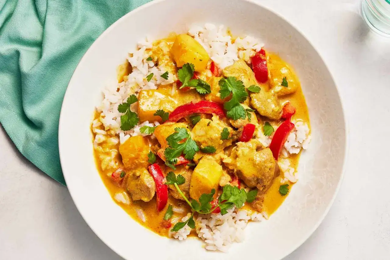 Aksamitne mango curry z kawałkami kurczaka, papryką i ryżem, udekorowane świeżą kolendrą.