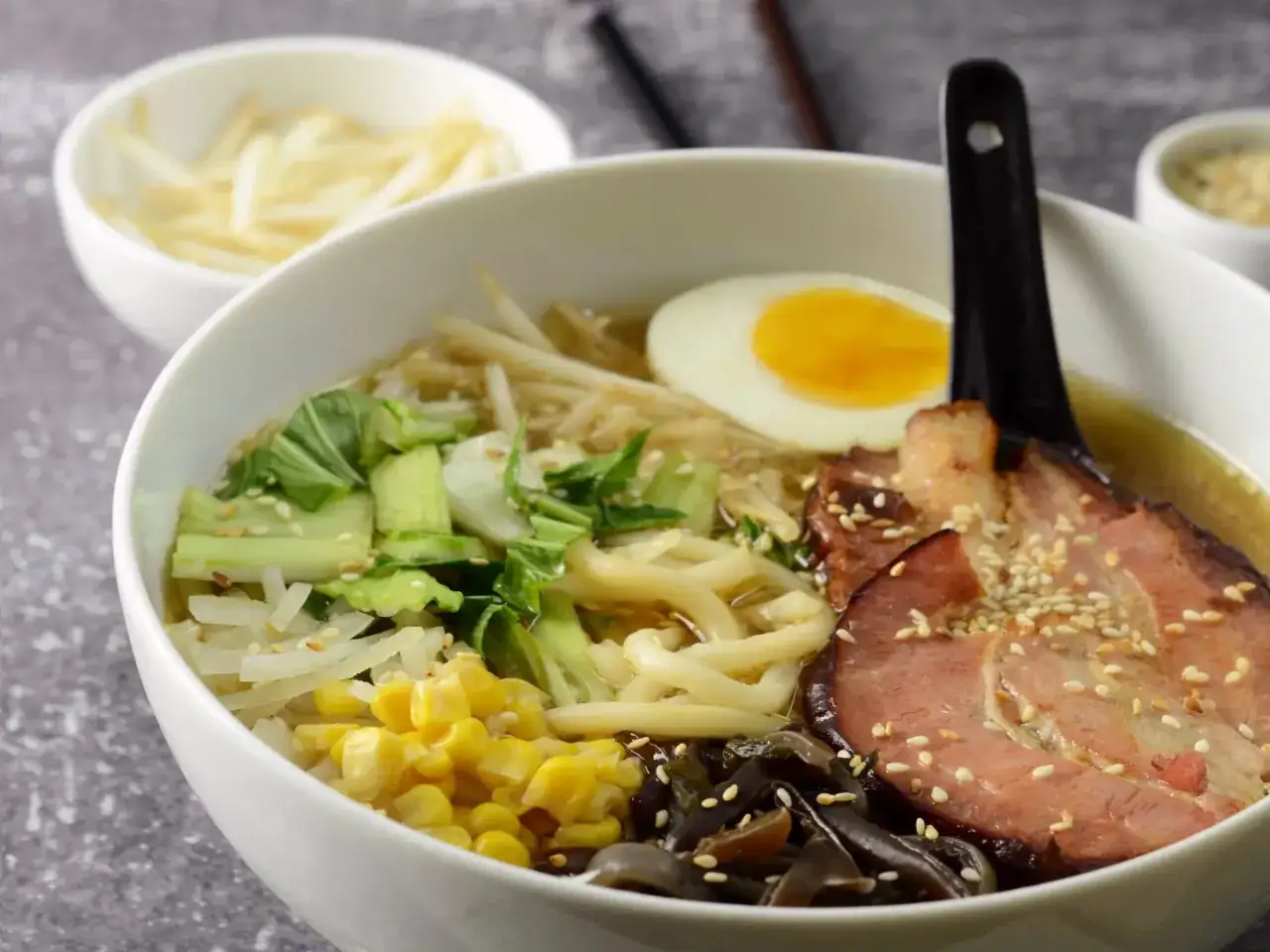 Pyszny ramen z kurczakiem, jajkiem na twardo, kukurydzą, warzywami i plastrami mięsa, posypany sezamem.