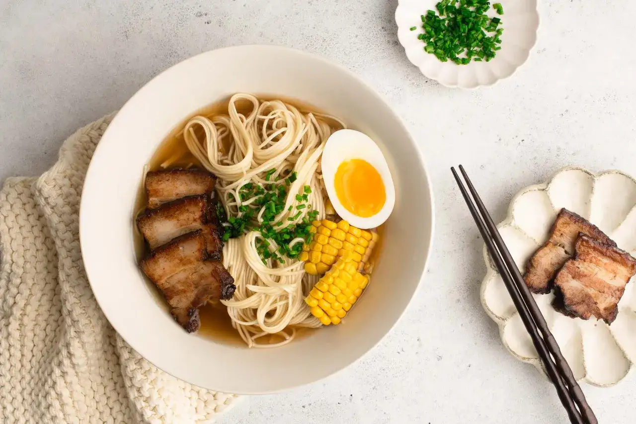 Miseczka aromatycznego makaronu ramen z sosem sojowym, plastrami boczku, jajkiem i kukurydzą.