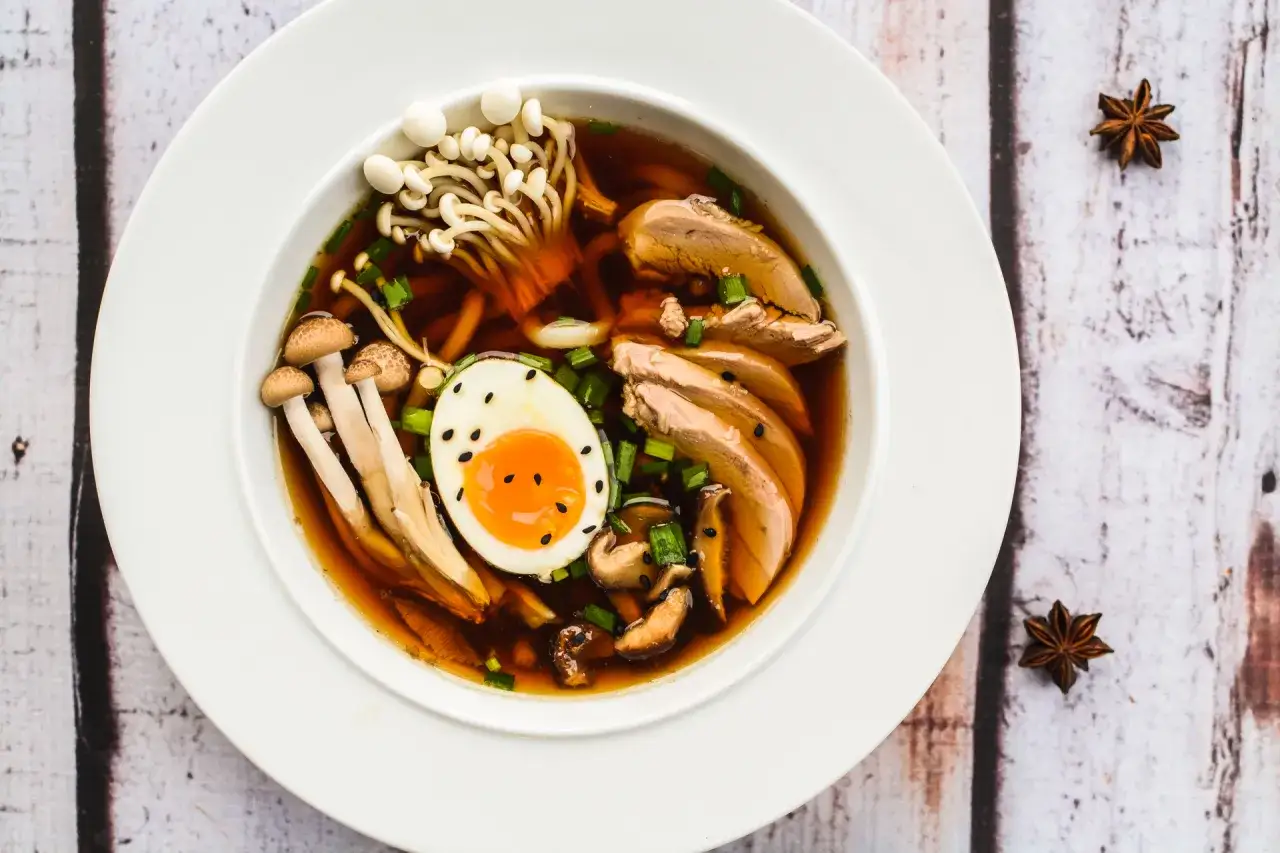 Aromaticzny ramen z kaczki z jajkiem na pół, grzybami enoki i shiitake, posypany szczypiorkiem.