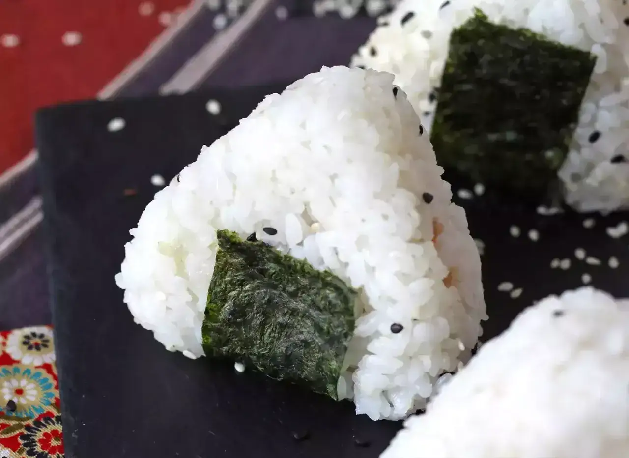 Trójkątne onigiri z tuńczykiem, ozdobione wodorostami nori i sezamem, wyglądają apetycznie.