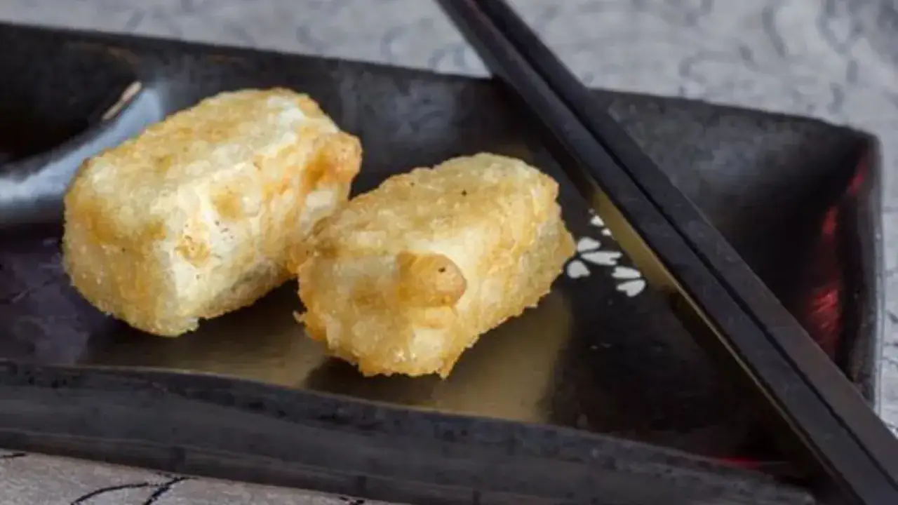 Chrupiące tofu w tempurze na czarnej zastawie, obok pałeczek. Idealna przekąska.